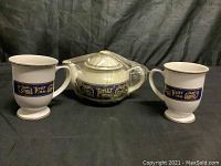 Two white ceramic Tetley Teas branded cups and a teapot arranged side by side showing front decorative bands