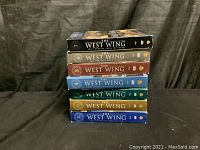 Seven stacked DVD box sets of The West Wing seasons 1-7 showing spine color and season numbering.