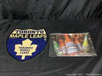 Photo shows Toronto Maple Leafs plastic sign and Budweiser metal sign side by side on black background.