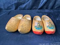 Two pairs of wooden shoes, one with carved ships, the other with painted windmills and red toes.