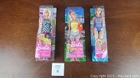 Three Barbie dolls in original packaging displayed side by side on wooden surface