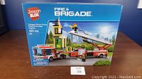 Front of the box showing the assembled fire truck, fire station, and firefighter figure with pieces count and age recommendation.