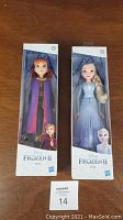 Photo of two boxed Frozen 2 dolls, Anna and Elsa, standing side by side on wooden surface.
