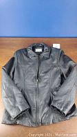 Front view of black leather womens jacket laid flat showing zipper and collar.