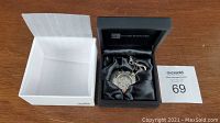 Mechanical pocket watch with chain in Things Engraved black satin-lined presentation box inside white outer box on wooden surface.