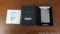 Photo showing boxed Zippo lighter with lid closed, exhibiting brushed chrome finish and box with Zippo logo.