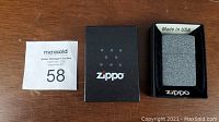 Top-down photo of Zippo Iron Stone lighter in original black Zippo box with numbered auction tag.
