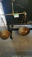 Full view of the antique brass balance scale hanging with two bow-shaped brass bowls suspended by chains on each side of the beam.