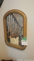Front view of the antique curved framed mirror mounted on a wall with dried branches in front reflecting in the glass. Reflects the room background.