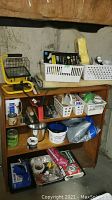 Wide view of wooden shelf with assorted baskets and hardware items including work lamp, gloves, cans, and other supplies.