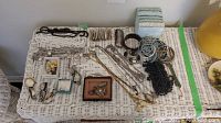 Wide view of the assortment of costume jewelry laid out on a white wicker table including necklaces, bracelets, brooches, watches, and cufflinks.