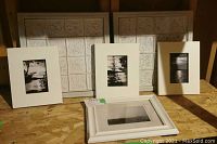 Four framed black and white photographs and two framed metal embossed tile art pieces arranged on plywood surface