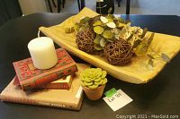 Photo of lot showing white pillar candle, decorative books, wooden tray holding woven balls and artificial greenery, and small succulent candle in terracotta pot.