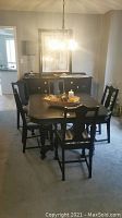 Full view of black dining table with five matching chairs in dining room, table holding a decorative centerpiece bowl and a candle.