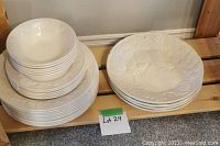 Stack of large, medium, and smaller plates along with a large serving dish, all white with embossed grape and leaf pattern