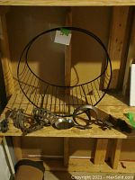 Front view of large circular metal log or blanket holder with vertical rods and various decorative metal sconces and attachment pieces displayed below.