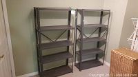Two metal shelving units with five shelves each, gray color, positioned side by side against a beige wall.