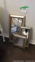 Three mirror wall décor pieces arranged on dark floor against wall, showing different sizes and metallic frames.