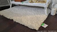 White faux fur rug placed under a white wicker table on dark wood flooring.