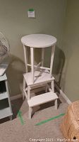 Photo of white wooden round table on top of two white wooden stools in corner of room