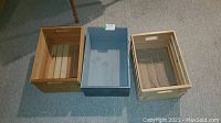Photo showing three wooden crates in different finishes and sizes placed side by side on carpeted floor.