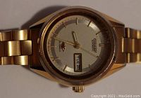 Front view of gold-tone Seiko automatic wristwatch showing day-date window on dial, linked wrist band, and gold-tone case.