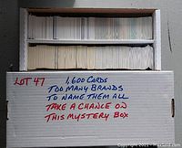 White cardboard box filled with 1,600 assorted trading cards viewed from top, showing varied card backs and handwritten note.