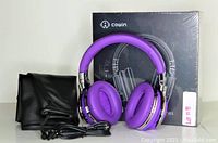 Photo of Cowin E7 headphones in purple with accessories and original box, displayed with carrying pouch and aux cable.