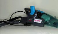 Photo showing a Bissell handheld vacuum cleaner in black and blue with power cord and nozzle attachment.