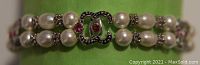 Close-up of a costume jewelry bracelet featuring double rows of faux pearls, rhinestones and an interlocking double-C logo centerpiece with rhinestones and pink stones.