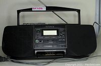 Sony black portable stereo with cassette player, radio tuner, dual speakers, and attached antenna, shown with handle extended and powering on.
