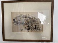 Framed black ink drawing on paper showing a village scene with figures and boats, signed with edition mark '1/6'.