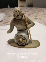 Front view of the carved sculpture showing the man holding a staff wearing a mask.