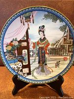 Front view of the collector's plate on a display stand showing the detailed painted scene of a traditional Chinese woman and floral elements.