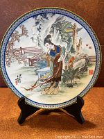 Front view of the painted collector plate showing Tai-Yu in a garden with floral and architectural elements, standing on a black stand.