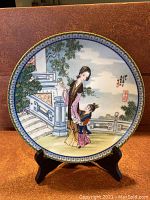 Front view of the decorative plate showing painted scene of a woman and child in traditional Chinese dress outdoors near architectural elements.