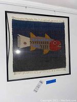 Full view of the square fish tapestry with vibrant colors, framed in black and displayed on a white wall.