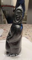 Side view of the black carved stone sculpture depicting a man holding a seal, showing details of the figure's parka and face.