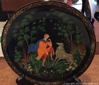 Photo showing front face of limited edition collectors plate with detailed painted scene of Tsarevich Ivan and Gray Wolf surrounded by forest and birds against a black background with gold decorative edging.