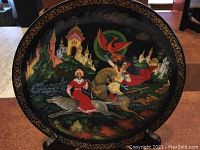Full view of the round collector's plate featuring Princess Elena and Ivan with the Firebird and a scenic backdrop on lacquer background.