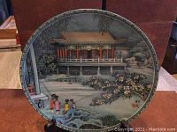 Front view of the decorative plate showing detailed painted scene with figures, traditional architecture, and floral elements.