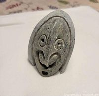 Front view of a small carved stone sculpture showing a stylized human face with large round eyes, nose, and mouth.