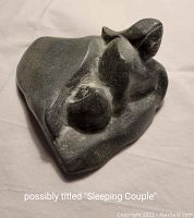 Top and side angle of the stone sculpture showing two abstract, reclining figures clasped closely, titled 'Sleeping Couple.'