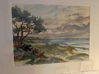 Photo of the watercolor coastal landscape painting with a tree, ocean and hills under cloudy sky, mounted on white backing.