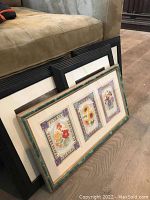Set of framed art leaning against couch including 3 black framed photographs and 1 green framed floral display.