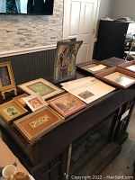 Wide angle photo showing 13 framed art pieces arranged on a dark wooden surface, varying in size from small to medium, mostly floral-themed and vintage designs.