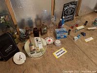 Overview of vintage barware and decor items arranged on floor including Jack Daniels sign, glass decanter, coasters, Chill Wizard box, and shot glasses