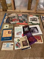 Photo showing collection of vintage magazines and books laid out on floor, with visible titles Life, American Home, McCall's and various books including home remedies and art.