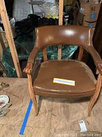 Full view of brown studded leather armchair with wooden frame and curved backrest.
