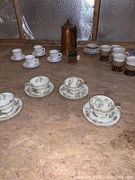 Photo showing all coffee cups and saucers arranged with copper coffee pot and small coffee grinder replica on a wooden surface